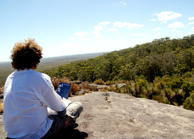 vorne links sitzt ein junger Mann mit dem GöTe in der Hand auf einem Felsen im Hintergrund ist eine Weitansicht von South Australia